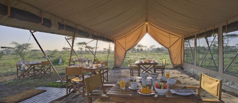 under a tent are tables and breakfast outside, behind them the savannah