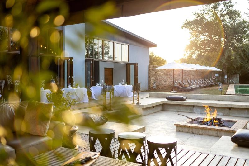 La terrasse du Karongwe Becks Safari Lodge, équipée de tables pour les repas en plein air, de fauteuils, d'un foyer extérieur et d'une piscine.