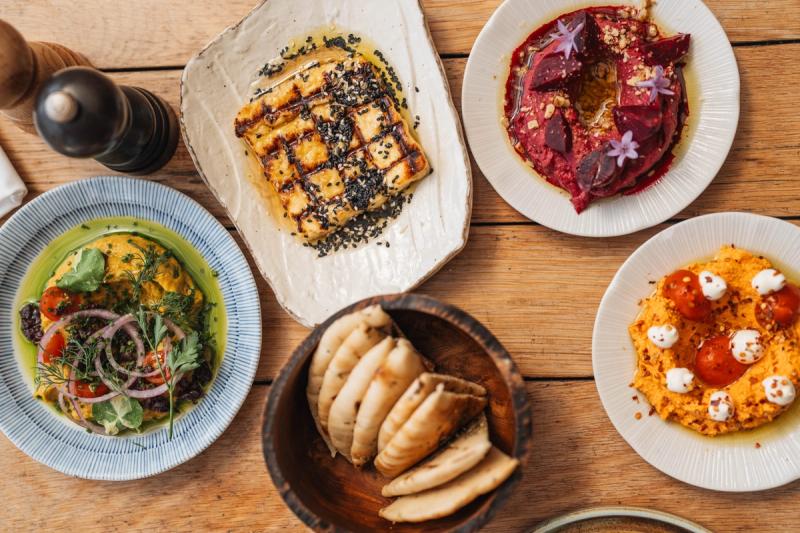 An array of small plates including pitas, grilled fish, salad, and colourful humus variations