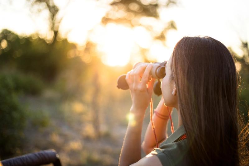 A woman lifts binoculars to the horizon