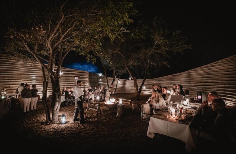 Guests enjoying an evening meal in Tanda Tula's open-air boma, illuminated by lanterns and a central fire beneath the African night sky.