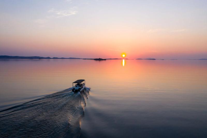 Boat cruising across Lake Kariba at sunset, with warm light stretching across the water.