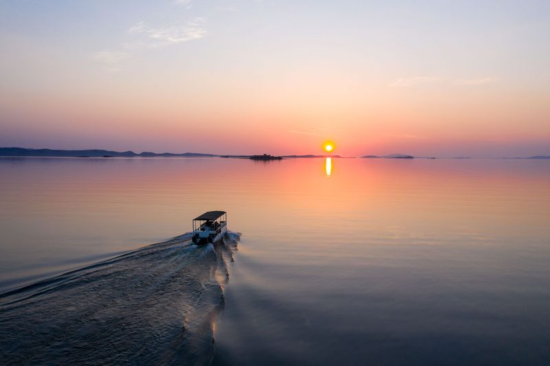 Boat cruising across Lake Kariba at sunset, with warm light stretching across the water.