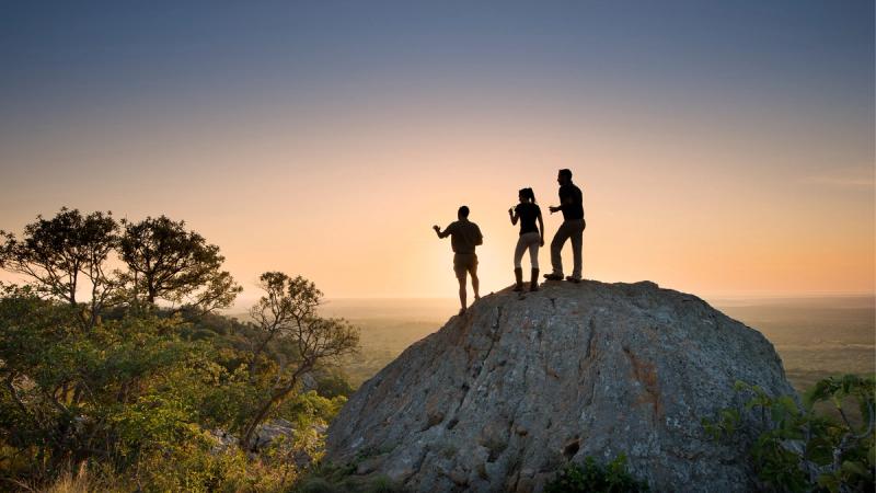 Silhouettes of people cast against a sunlit rock at sunset