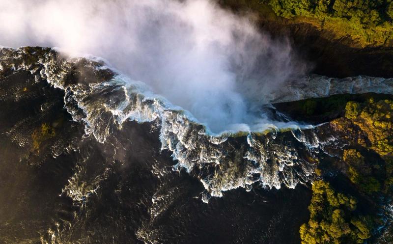 A dramatic aerial view shows torrents of water plunging into mist, capturing the sheer power and scale of the best side of Victoria Falls.