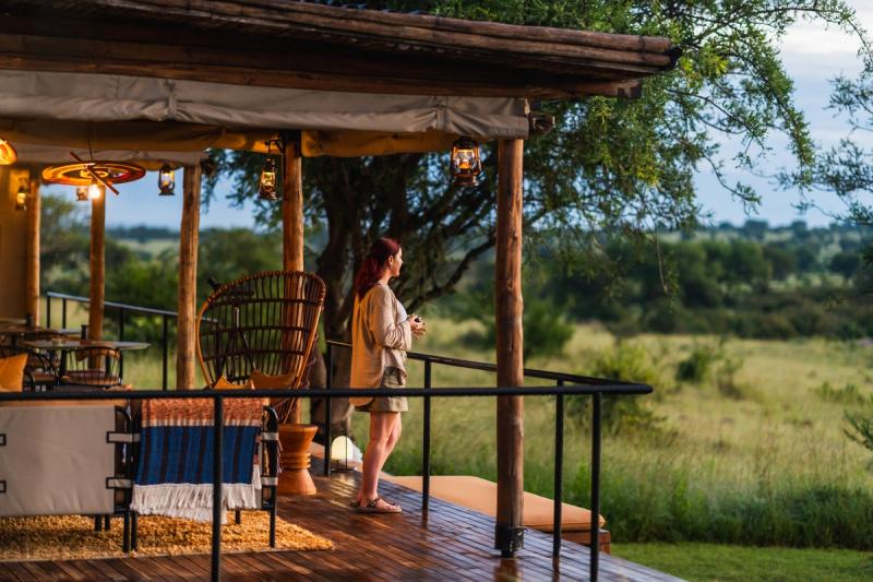 A woman stands on a lodge deck overlooking the savannah, highlighting how safe are safari tours with thoughtfully designed accommodations.