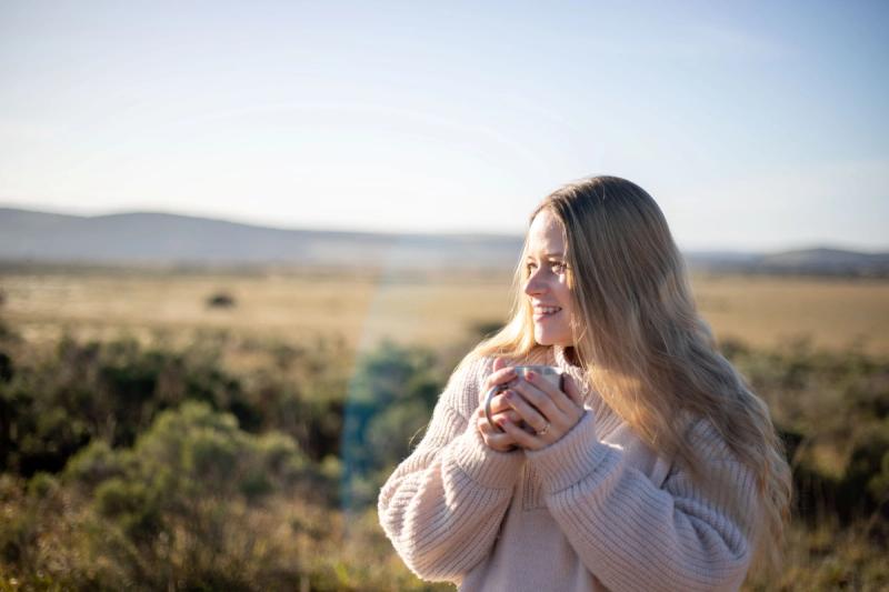 Katharina in a cosy sweater holds a warm cup of tea, smiling as she gazes out over the vast African savanna during her babymoon safari.