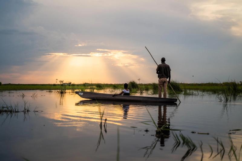 A guide poles a traditional mokoro canoe through the calm waters of the Okavango Delta at sunset, offering a serene perspective on why this is the best time to visit Botswana for a safari.