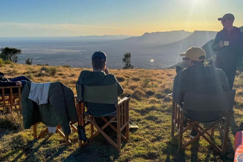 David and friends sit in chairs on a hilltop, enjoying the Karoo sunset over the expansive valley.