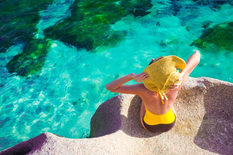 Woman in sun hat and swimsuit relaxing on the rocks over the sea Seychelles