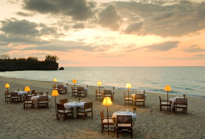 Auf einem Strand stehen viele Tische und Sesseln, daneben das Meer
