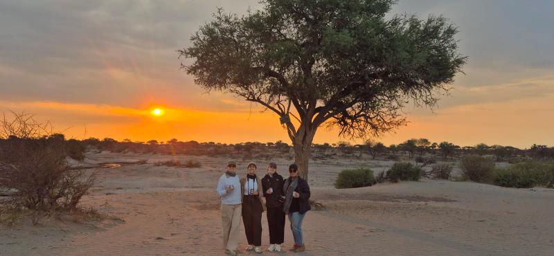 Four travellers enjoy a drink in front of a sunset in Botswana