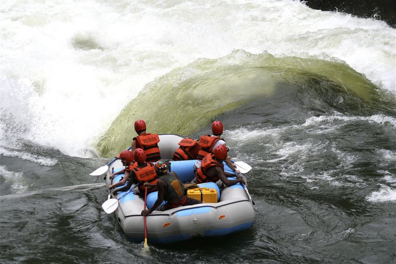 A raft full of helmeted adventurers paddles toward a surging rapid near the best side of Victoria Falls.