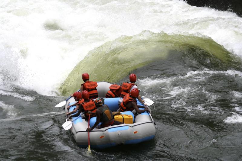 A raft full of helmeted adventurers paddles toward a surging rapid near the best side of Victoria Falls.