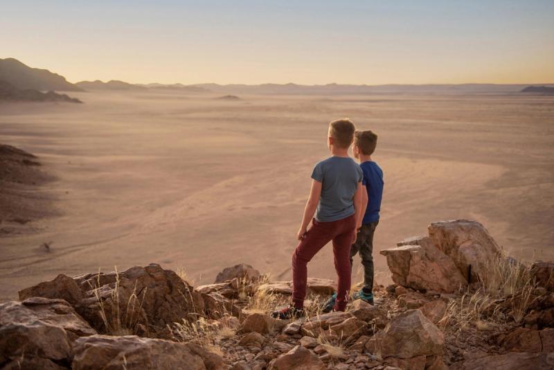 Two boys stand on a rocky outcrop overlooking the vast Namib Desert, capturing how remote the best destinations for kids can inspire big adventures and bigger imaginations.