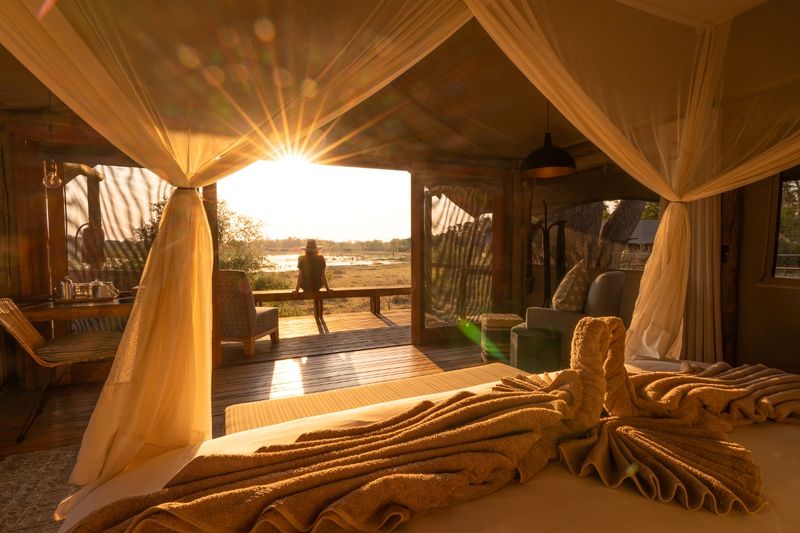 Golden morning light spills into a canvas tent as a guest looks out over a peaceful floodplain