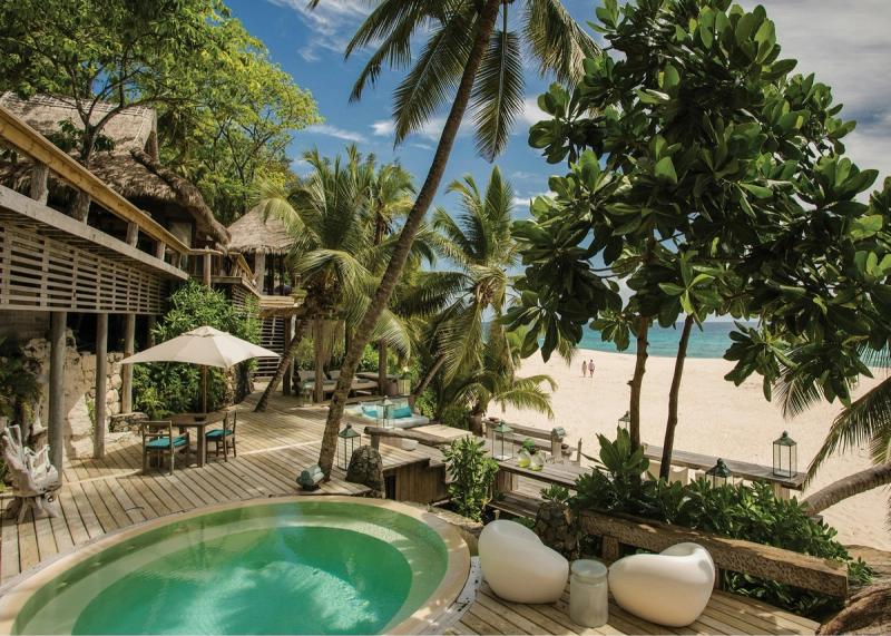 A luxurious beachfront villa with lush greenery, a private pool, and a serene view of a white sandy beach and turquoise ocean