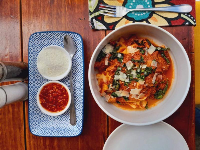 A bowl of Italian pasta with a chili sauce and parmesan cheese on the side.
