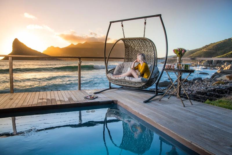 A woman sits on a hanging chair overlooking the ocean and mountains at one of the luxury hotels in Cape Town