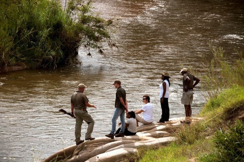Safari-Urlauber auf einer Buschwanderung im Lion Sands Game Reserve an einem Fluss