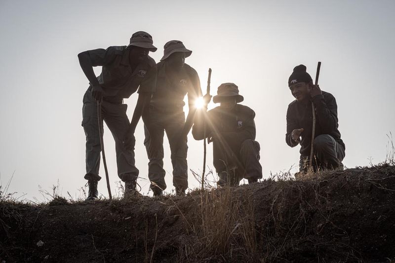 Rhino Guardians from the Tracker Academy stand silhouetted against the sun as they observe the landscape during field training.