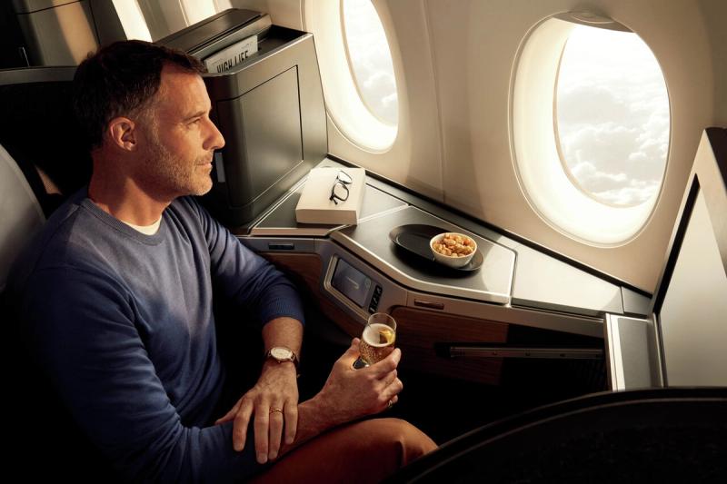 A traveller enjoys a glass of champagne in a spacious and elegant first-class cabin, complete with a stunning view of the clouds.