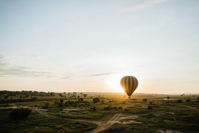 A hot air balloon drifts over golden plains at sunrise during a safari in October.