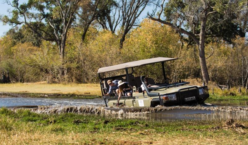 A safari vehicle splashes through a shallow water crossing as guests reach out in delight, capturing a manifesto moment shaped by motion and spontaneity.
