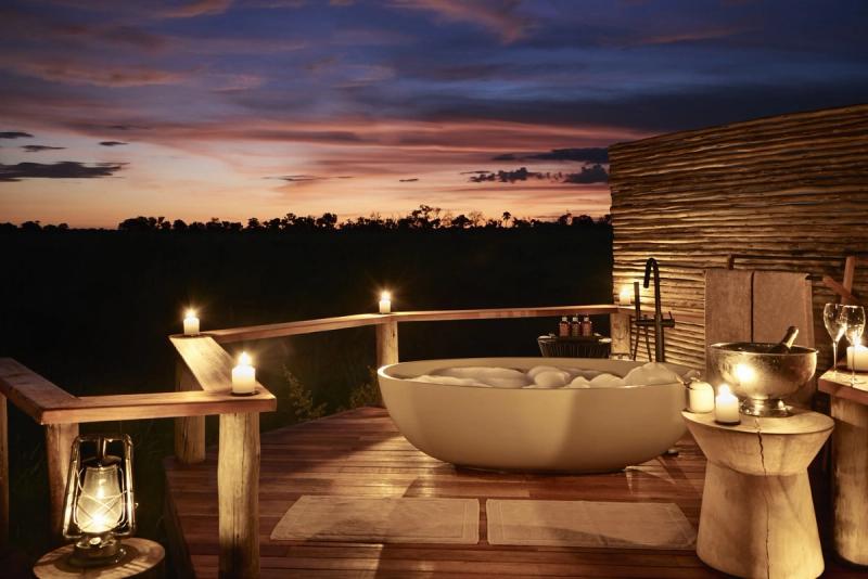A luxurious outdoor bathtub surrounded by softly glowing candles on a wooden deck is a dreamy setting for your romantic safari in Africa