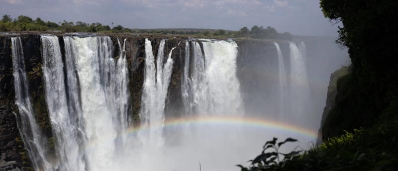 Victoria Falls thundering into the gorge with mist and a rainbow rising from the spray.