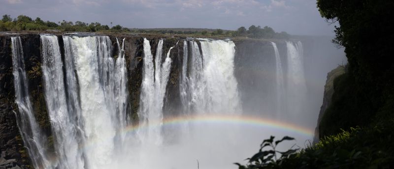 Victoria Falls thundering into the gorge with mist and a rainbow rising from the spray.