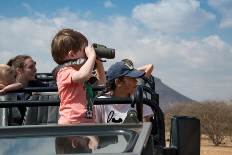 A young child peers through binoculars on a safari vehicle, perfectly capturing how the best destinations for kids can introduce the wild in safe, exciting ways.