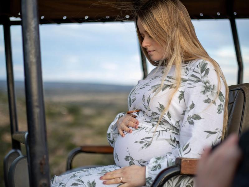 Katharina sits in an open safari vehicle, cradling her baby bump while gazing out at the vast African wilderness during her babymoon safari.