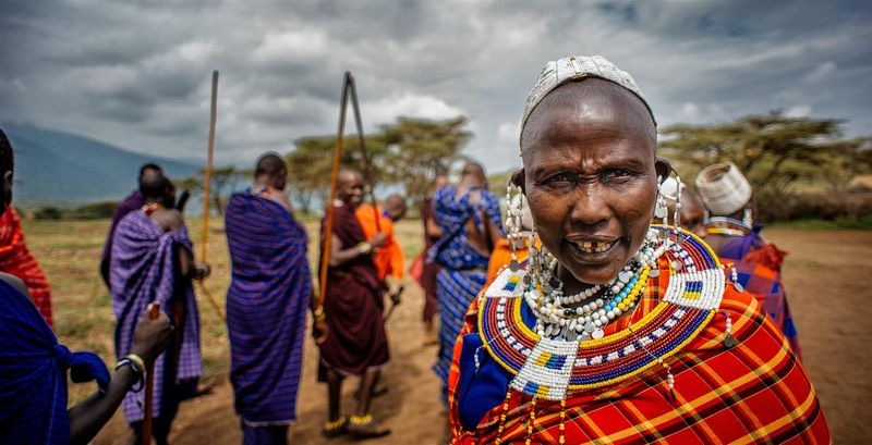 A group of Maasai people in vibrant traditional dress stand outdoors, with one woman in the foreground wearing elaborate beaded jewellery – a cultural encounter that speaks to the best time to visit Kenya.