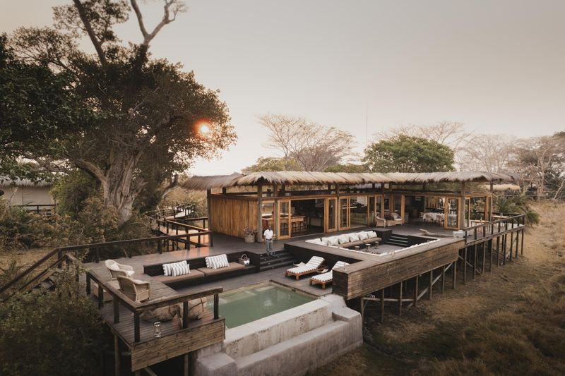 An elevated wooden safari lodge with a pool and open-air lounge overlooks the grasslands of Zambia’s Busanga Plains at sunset