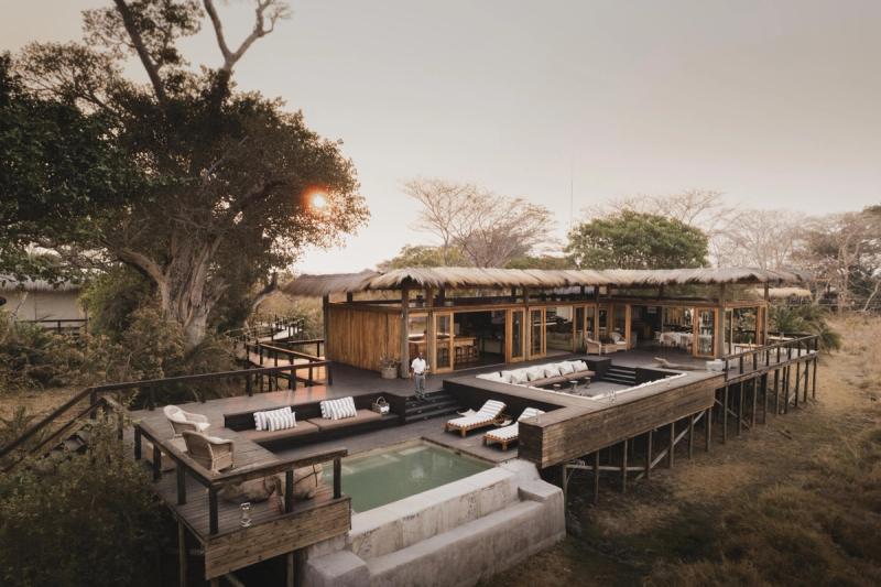 An elevated wooden safari lodge with a pool and open-air lounge overlooks the grasslands of Zambia’s Busanga Plains at sunset