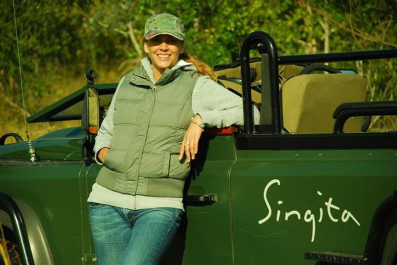 A woman stands in front of a game vehicle while staying at Singita on a safari