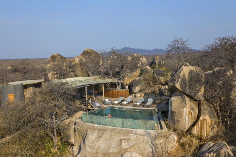 An infinity pool carved into granite boulders overlooks vast, dry Ruaha wilderness, capturing the dramatic setting of Luxury safari lodges in Tanzania.