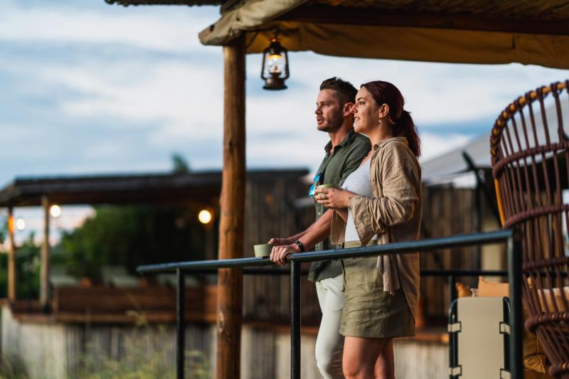 A couple stands on a lodge deck with coffee in hand, illustrating how safe are safari tours when every detail is carefully managed.