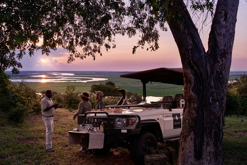 A guide chats with guests at a sundowner stop overlooking a meandering river