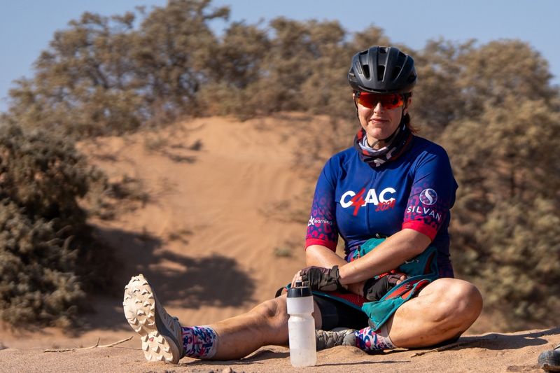 Kitted out with cycling gear, Michelle sitting in the sand alongside a dune