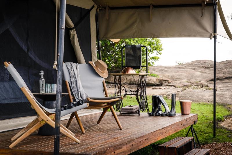 A private deck at one of Tanzania’s mobile tented camps is styled with canvas chairs, leather boots, a vintage sewing table, and safari essentials.