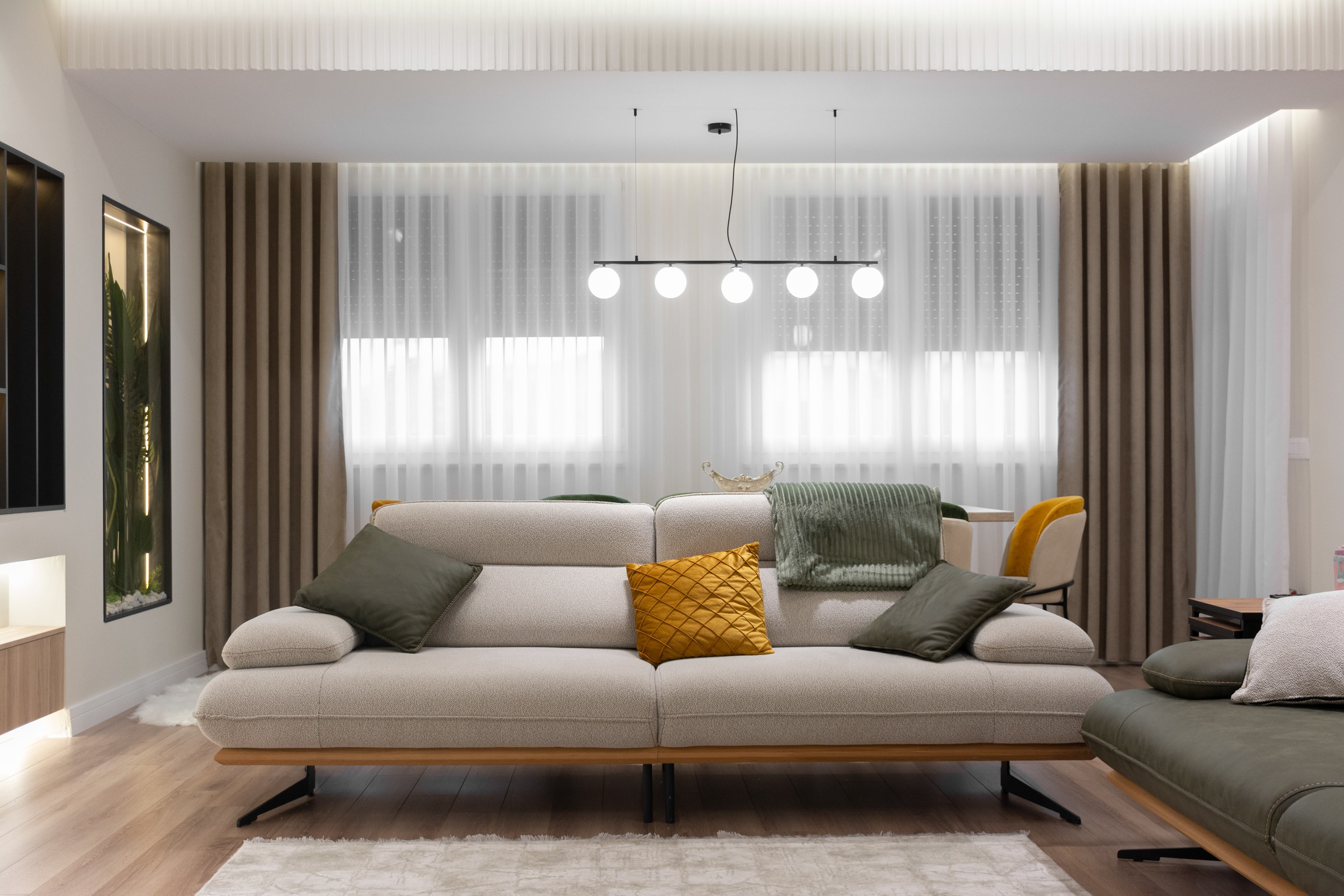 Living room with beige and green sofa, sheer curtains and globe pendant light, apartment in Gostivar
