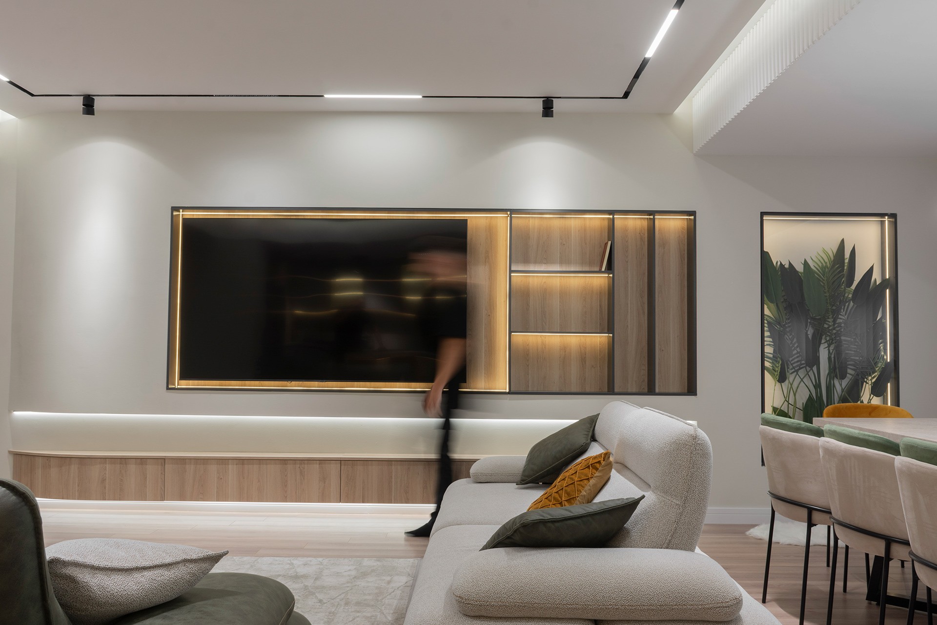 Beige sofa with green and mustard cushions in front of a lit TV wall, apartment in Gostivar