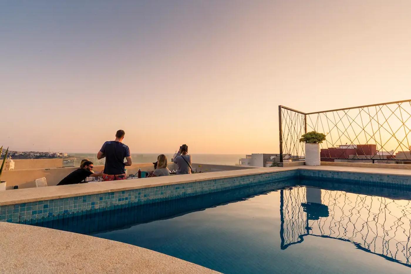 Gäste essen bei Sonnenuntergang gemeinsam auf einer Dachterrasse in Tamraght, Marokko