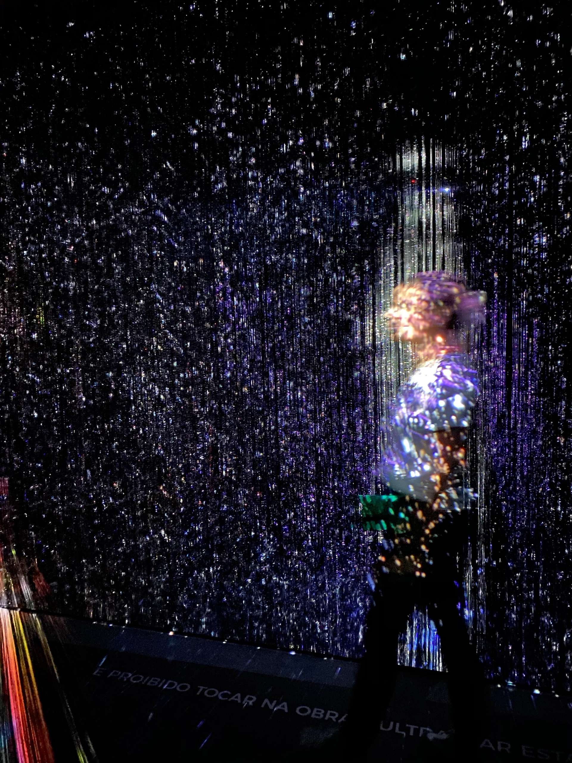 A woman is seen blurry through various streams of light, in this photograph of a viewer interacting with a work by Maja Petric