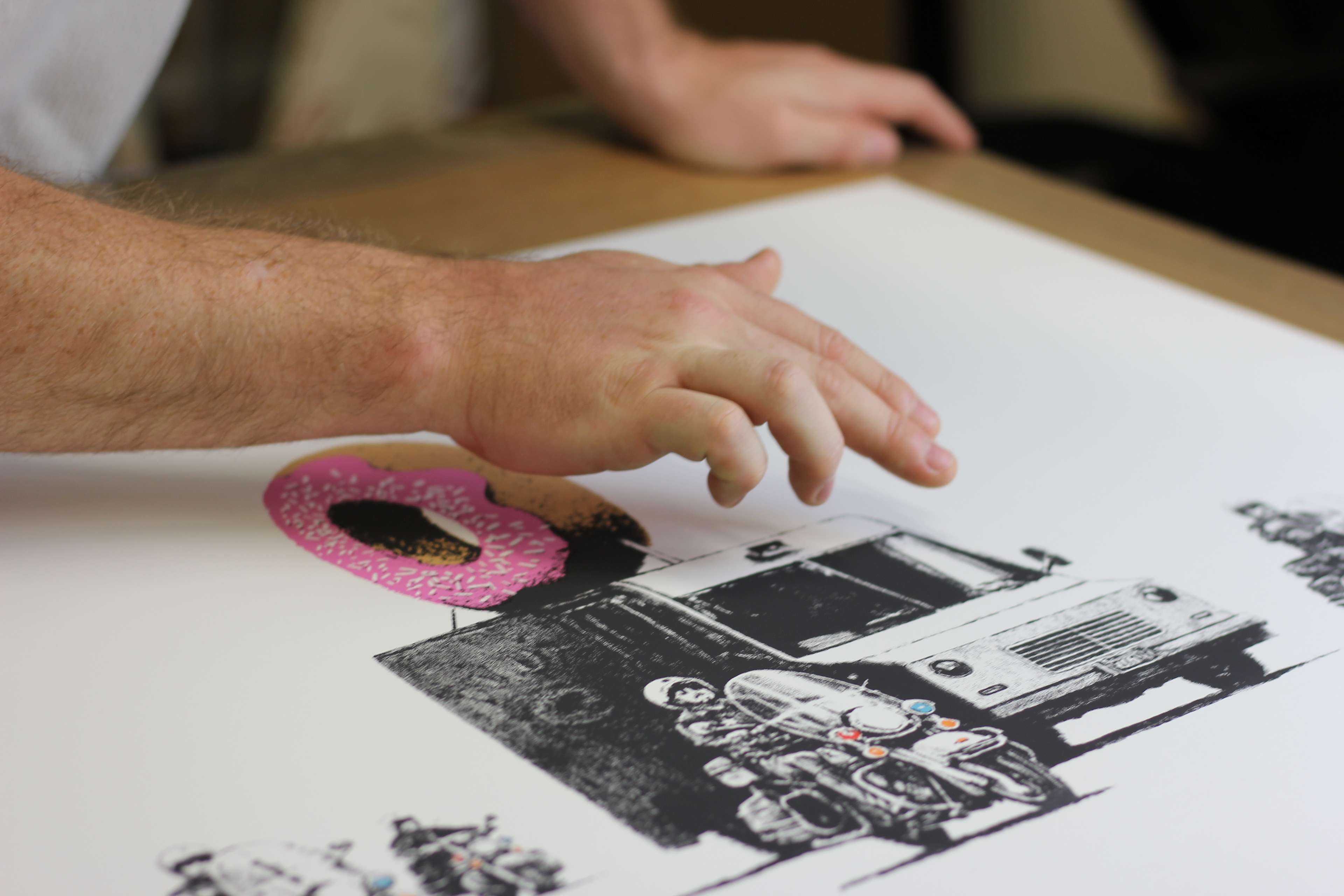 A photograph of a hand pointing at an artwork depicting a police van with a red doughnut on its roof.