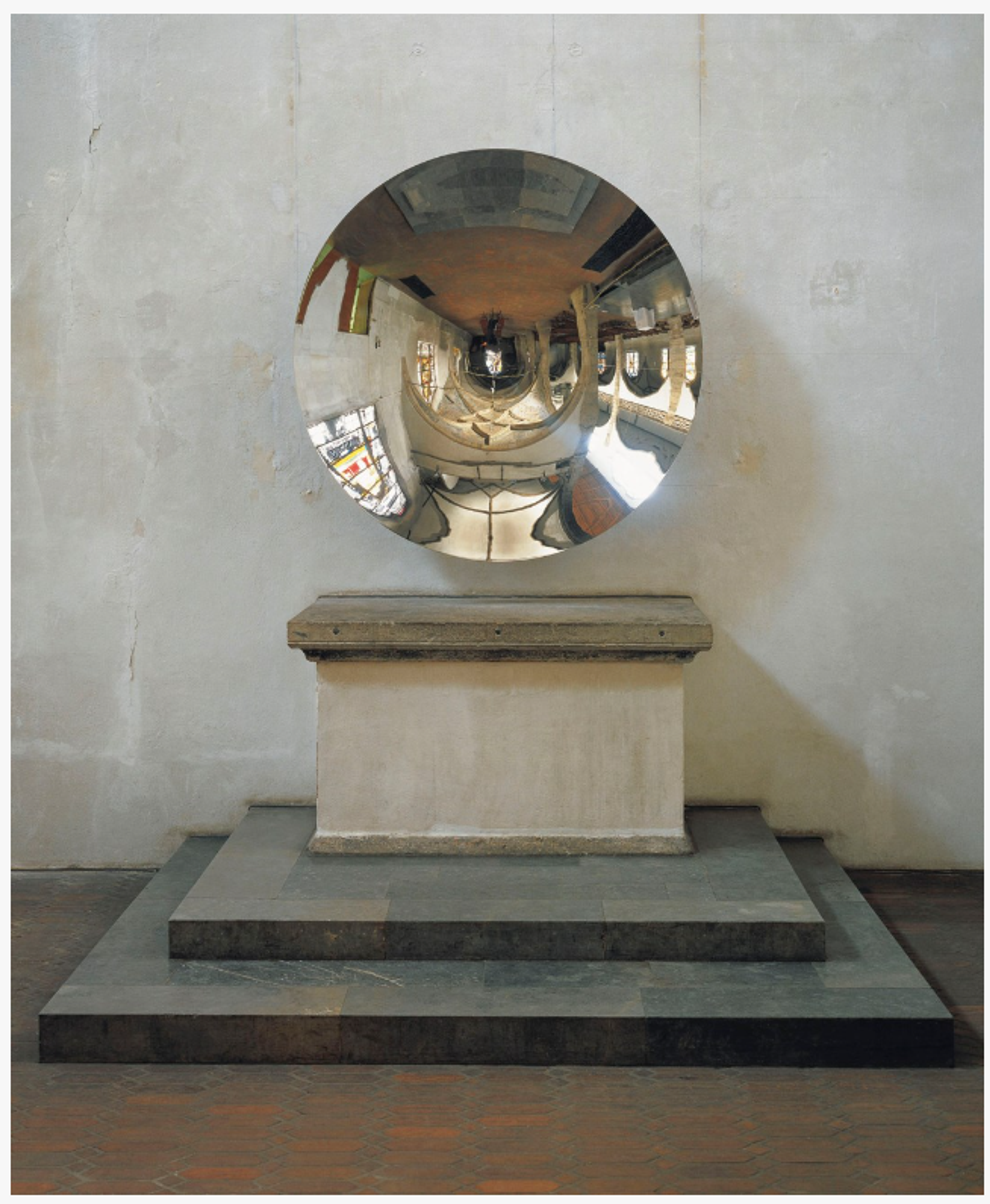 A spherical stainless steel mirror on a stone pedestal, creating distorted reflections of its grand surroundings.