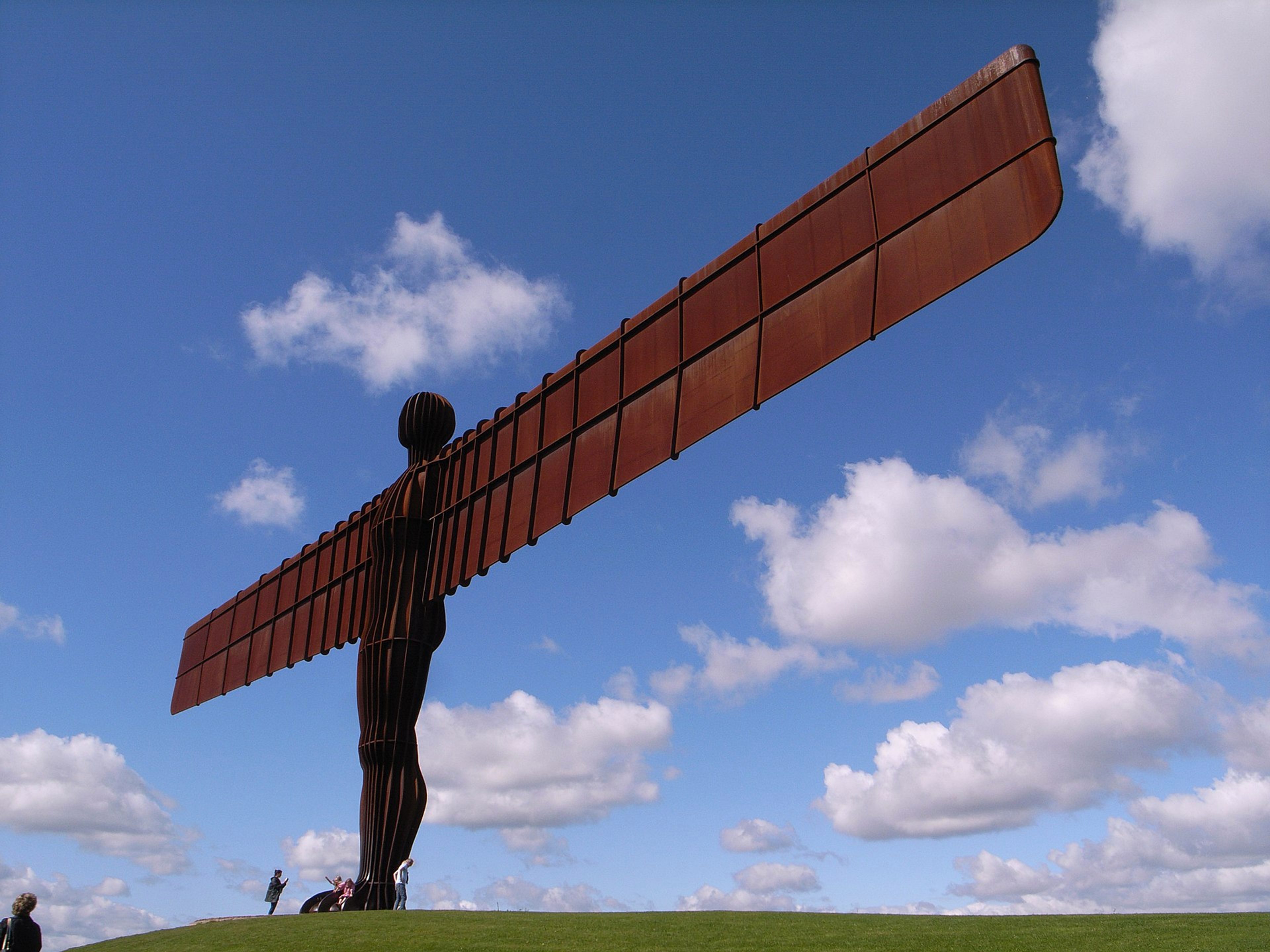 A photograph of Antony Gormley's giant Angel of the North sculpture, a human figure with giant wings for arms, against a sunny sky.