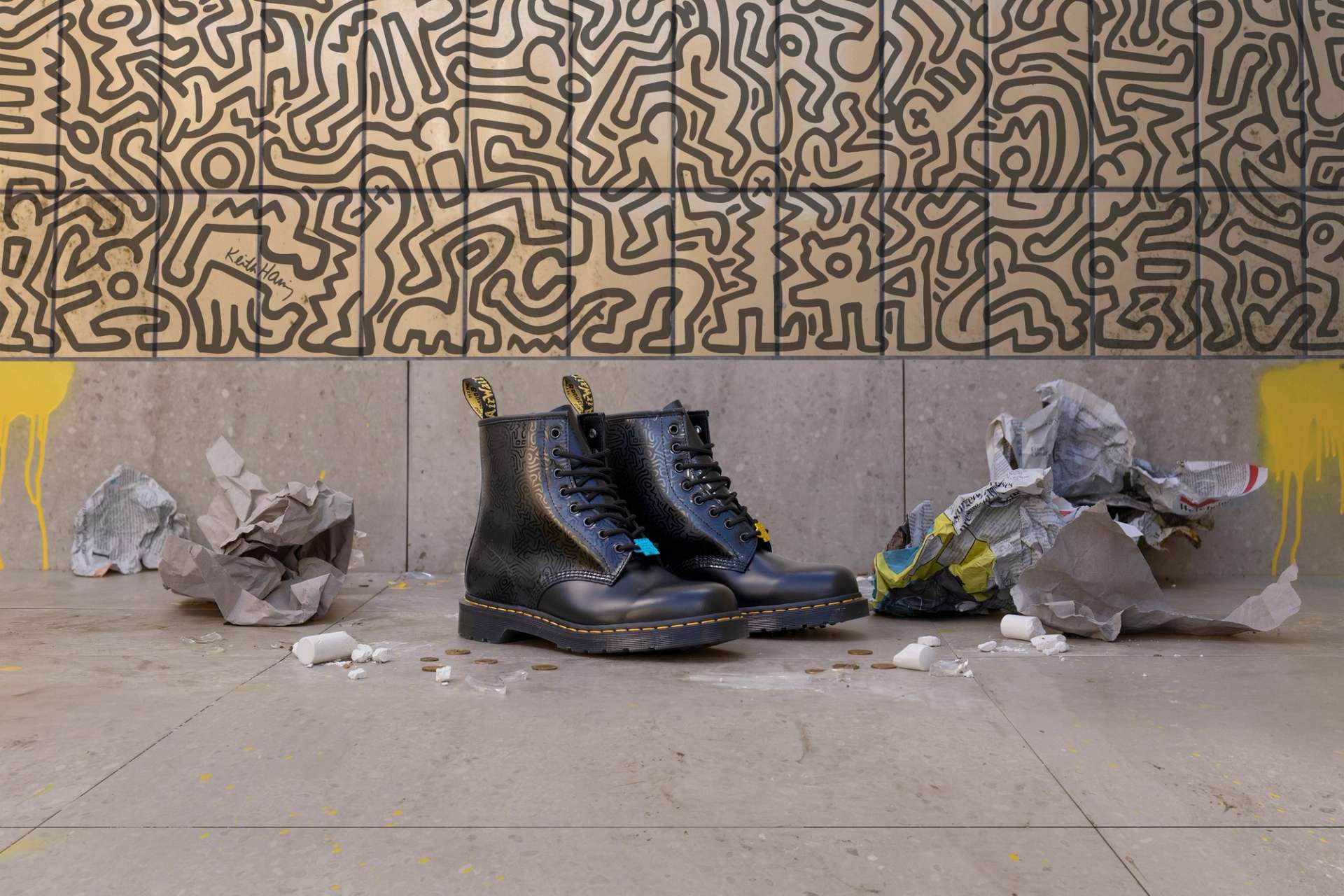 A photograph of a pair of boots from Dr. Martens’ collaboration with Keith Haring, placed against a background featuring one of the artist’s iconic murals.